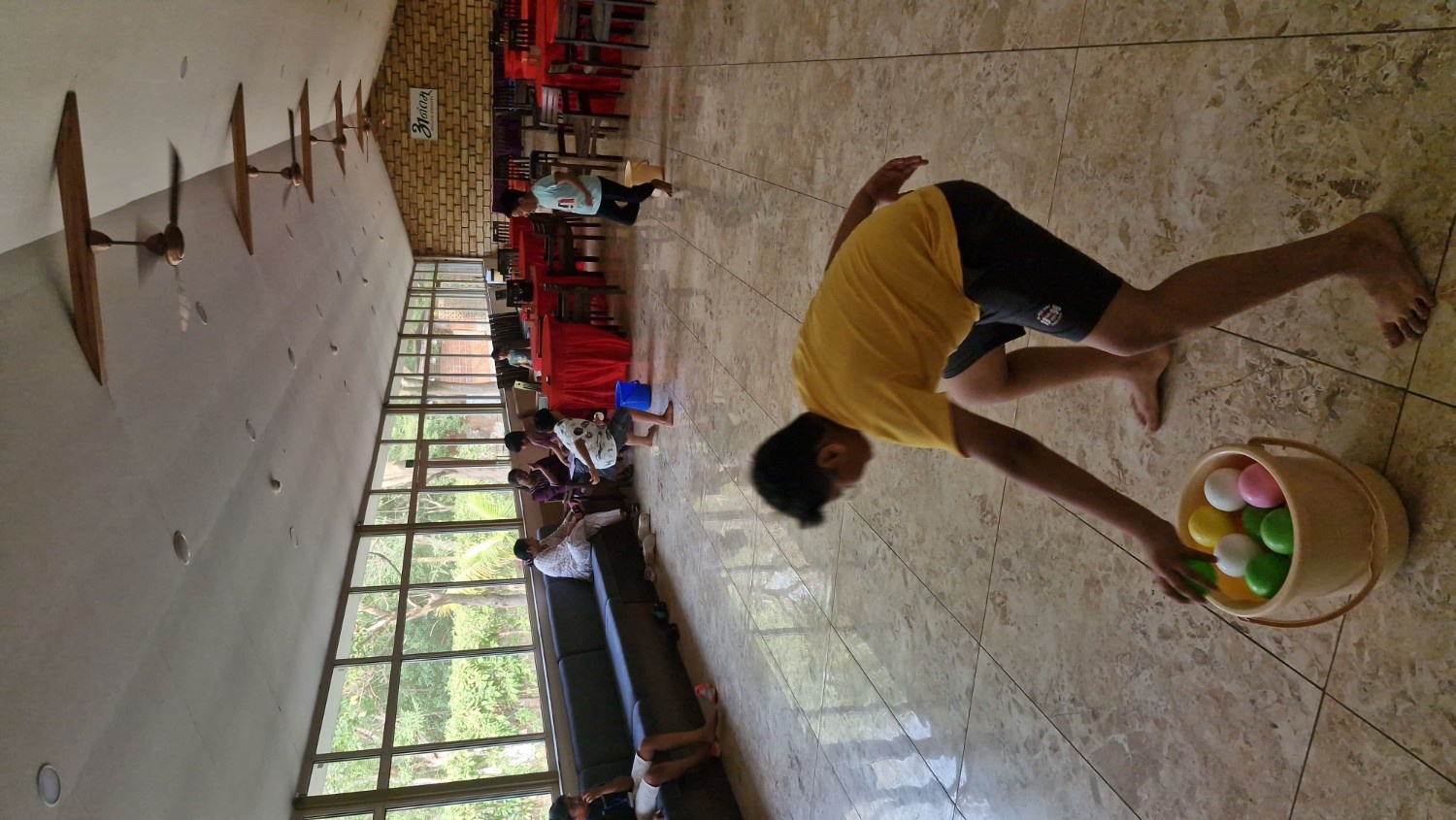 A boy reaching into a bucket of colorful plastic balls during an energetic indoor summer camp game