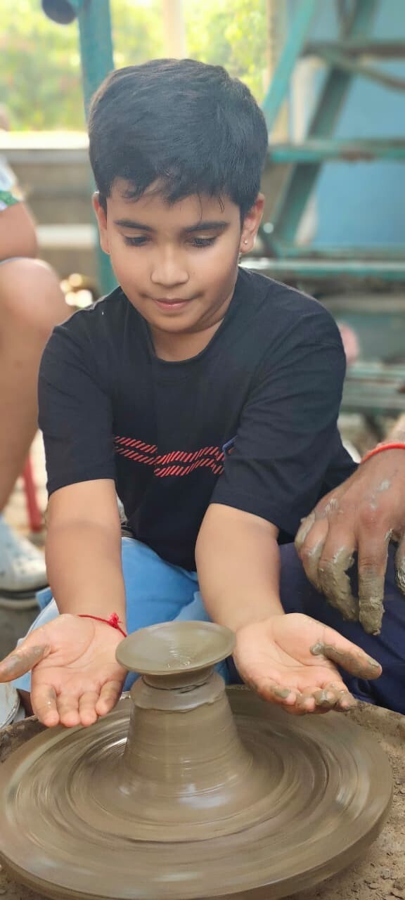 A young boy holding out his muddy hands after shaping a clay pot on a pottery wheel