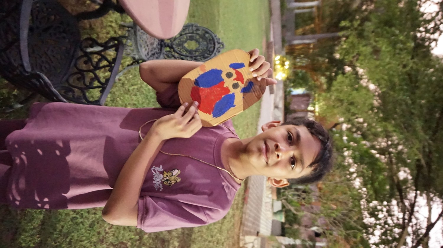 A boy in a purple shirt proudly holding up a cardboard craft painted to look like a red and blue owl