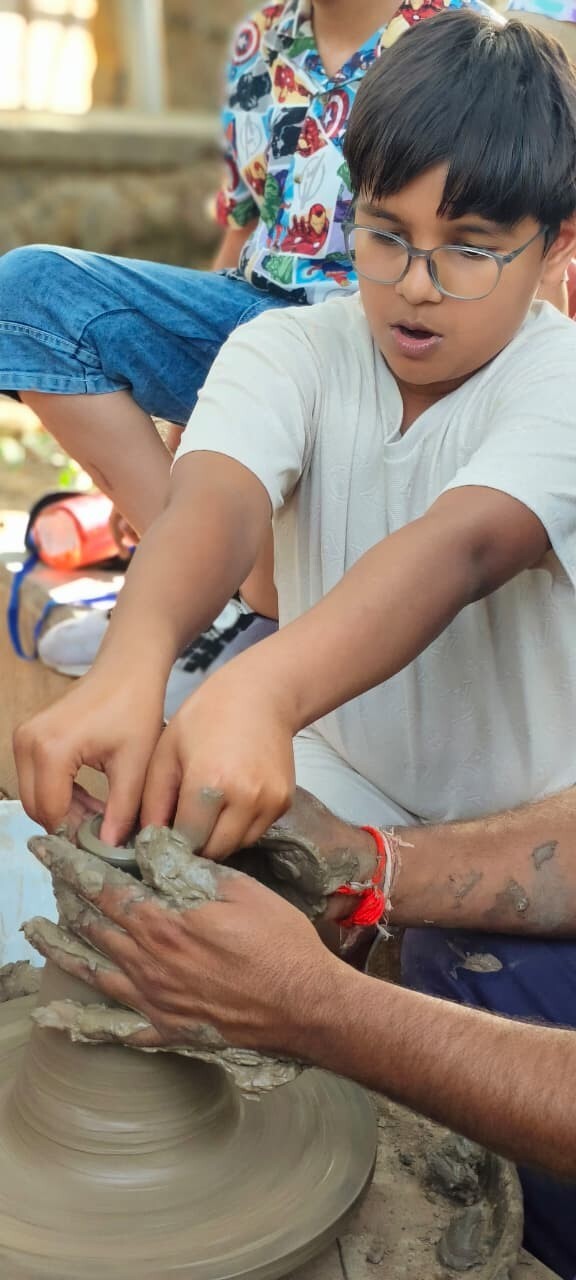 A boy with glasses focusing closely as he shapes a clay pot on a spinning wheel