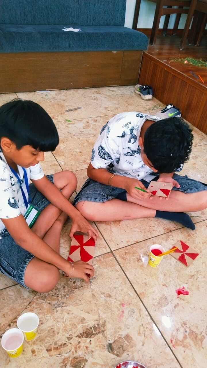 Two boys sitting on the floor carefully painting red triangles onto square cardboard tiles