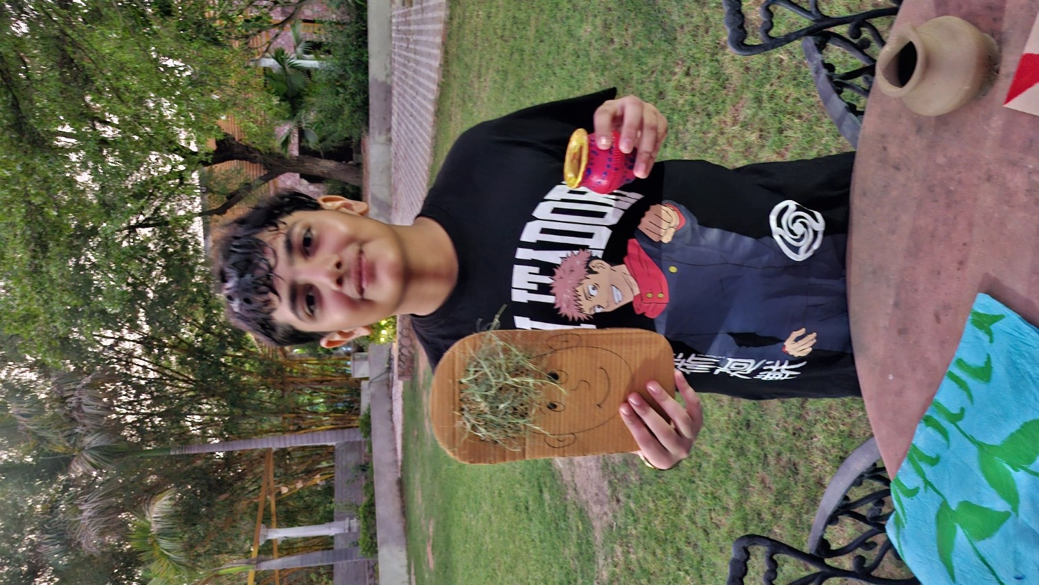 A summer camper holding up a cardboard face craft with grass hair and a small brightly painted clay pot