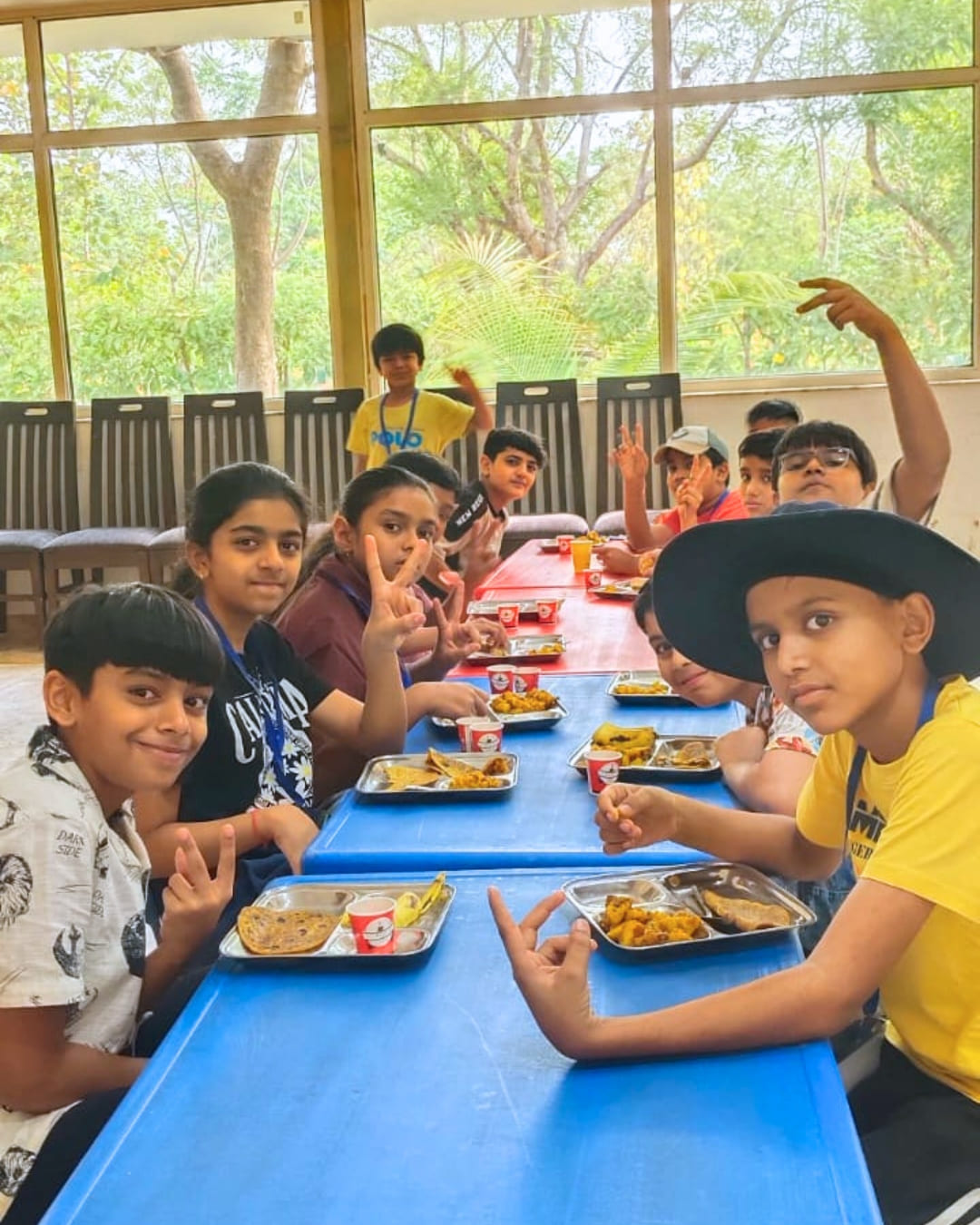 A group of happy kids sitting together at a long blue table, enjoying a meal from metal trays