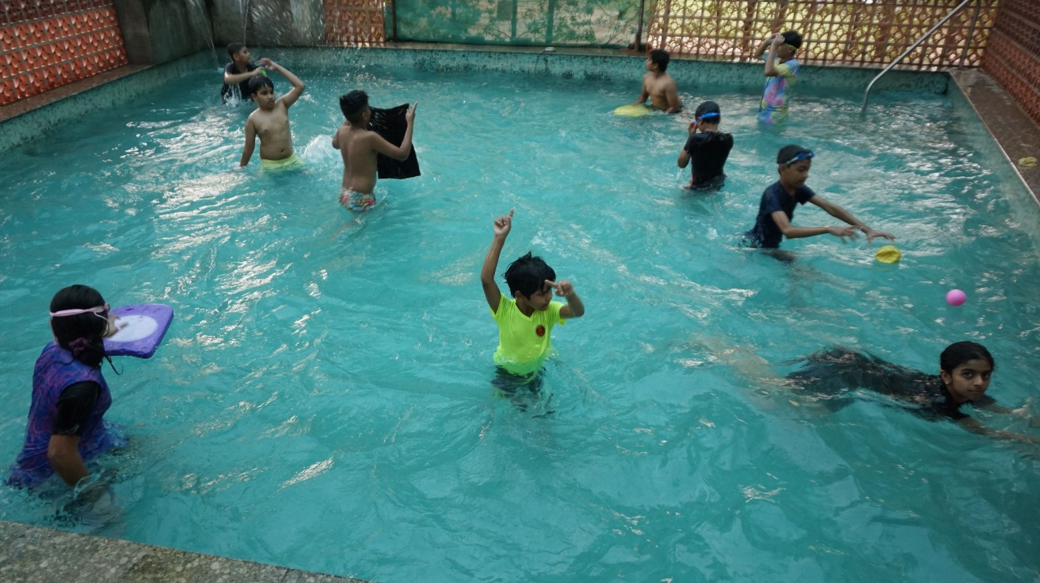 A group of kids having a great time swimming, splashing, and playing with balls in an outdoor pool