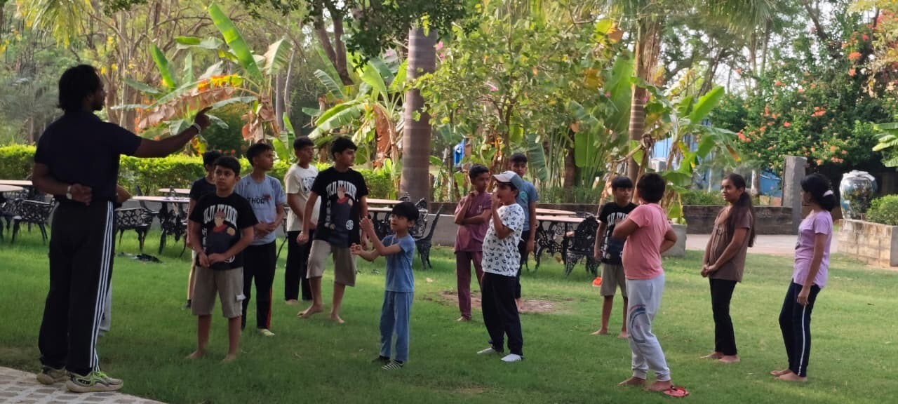 A summer camp instructor giving directions to a group of kids standing on the grass