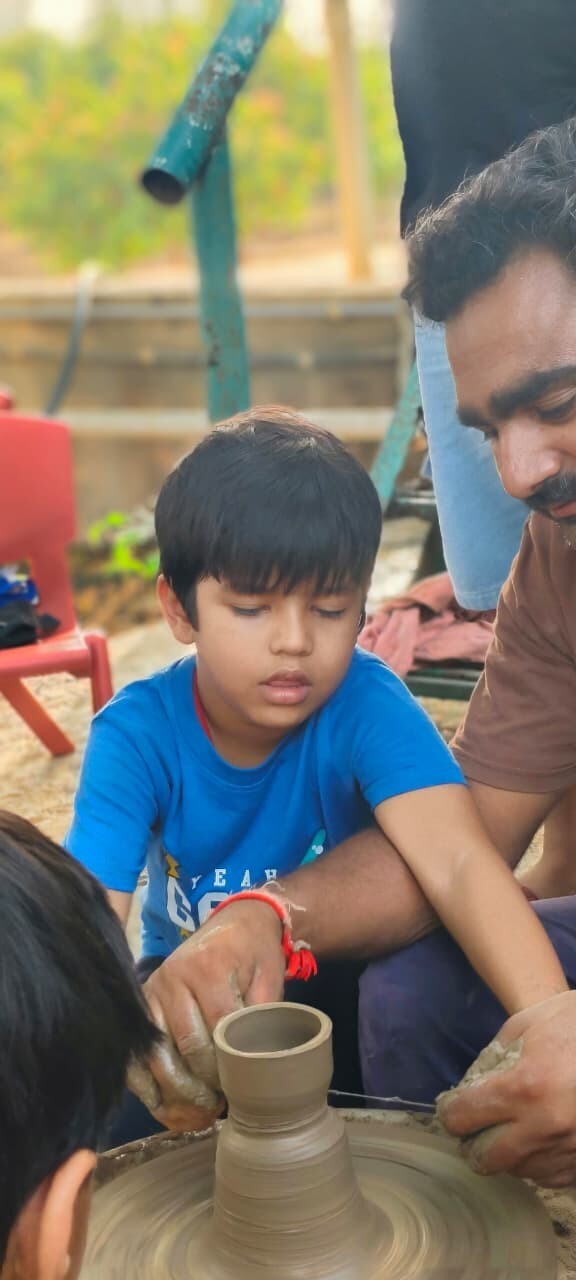 A summer camp instructor guiding a young boy's hands as he shapes clay on a pottery wheel