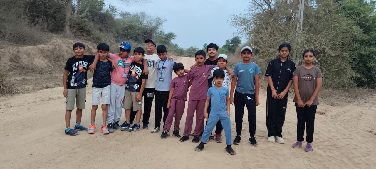 A group of children standing together with their arms around each other for a photo on a sandy dirt path