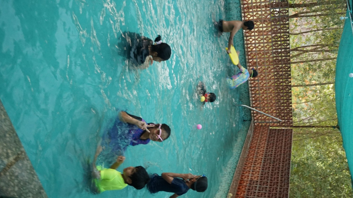 A group of children having fun, swimming, and playing with balls in an outdoor pool