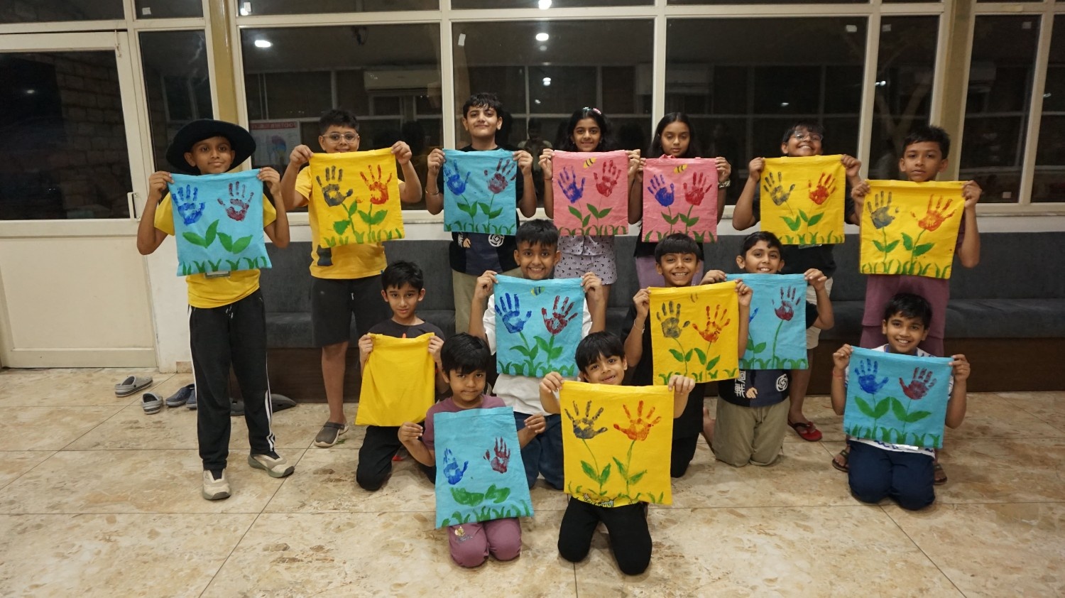 A group of children proudly holding up colorful canvas tote bags they painted with bright handprint flower designs
