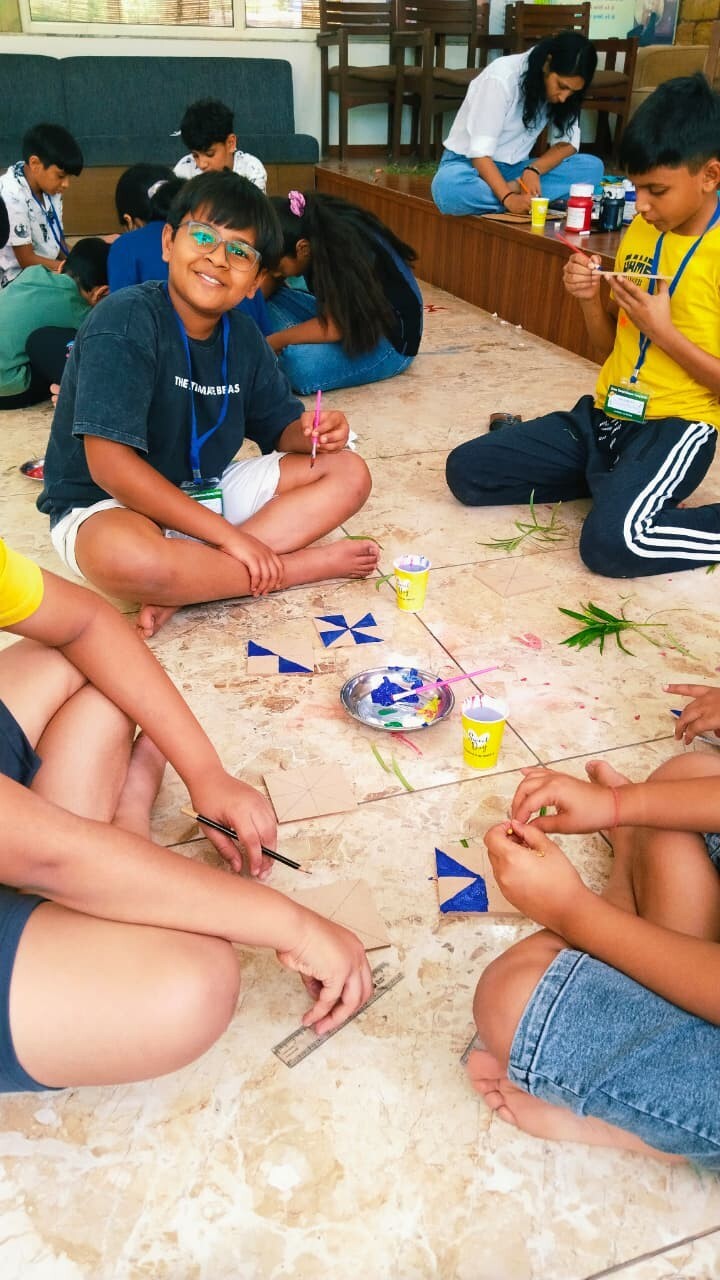 A smiling boy with glasses painting blue geometric patterns on cardboard tiles