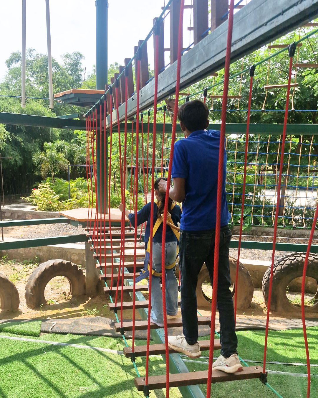 Instructor guiding a child on a suspension rope bridge at adventure campsite
